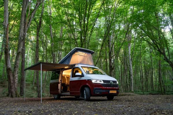 Ormanda yan kapısı açık, iç aydınlatması görünen bordo-beyaz Demonte Karavan campervan