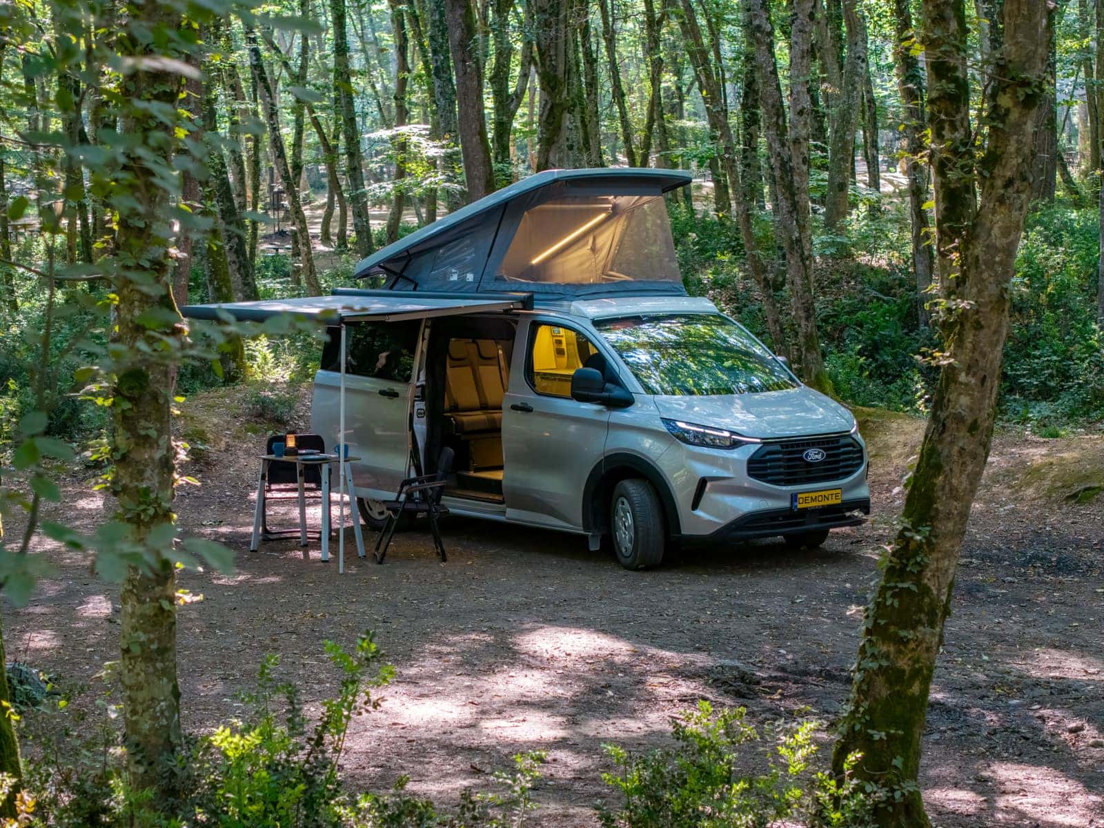Ford Transit Custom tabanlı Assos ormanda; pop-up tavanı ve tentesi açık, kamp masası kurulu